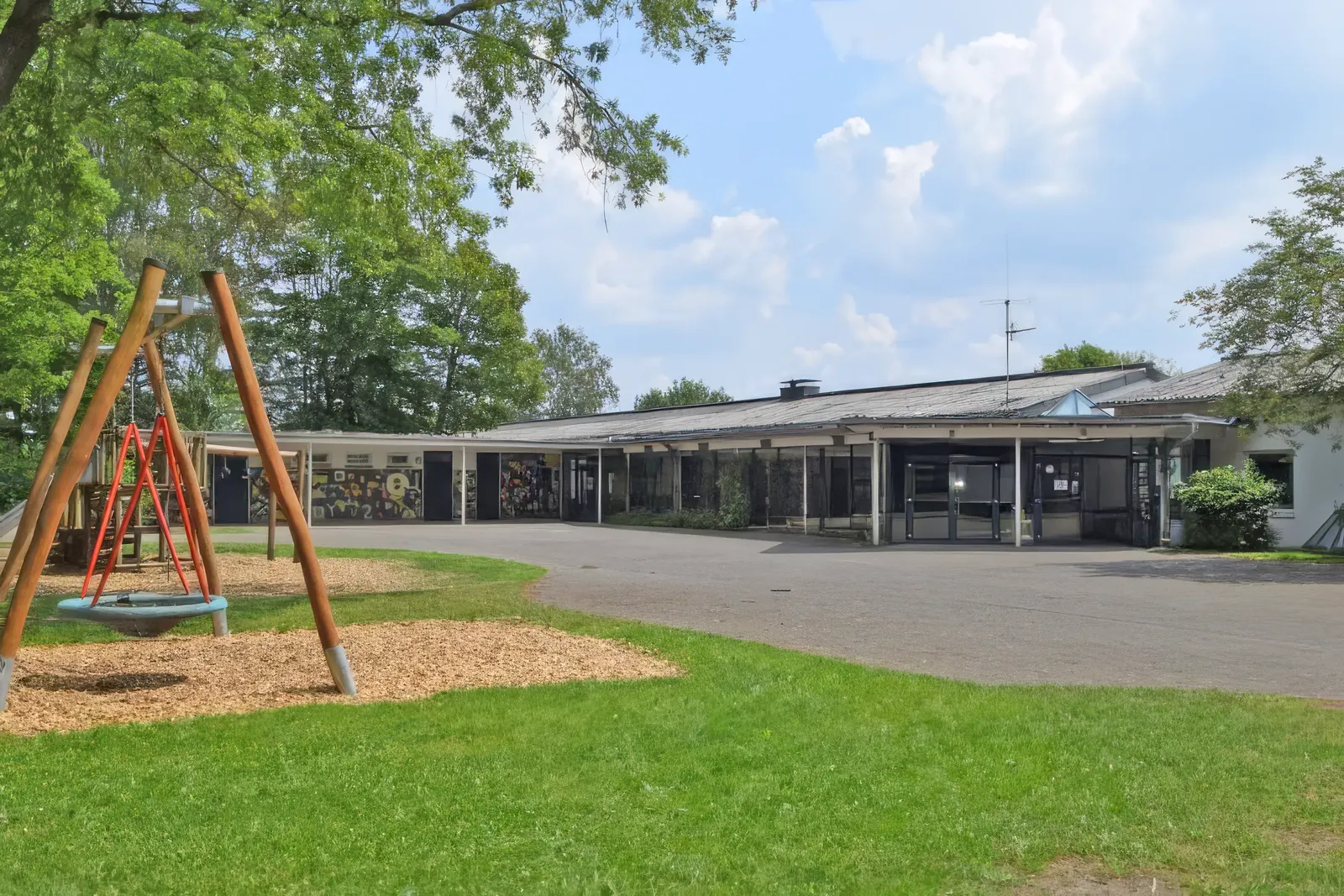 Schulgebäude und Schulhof der GGS Auf dem Höchsten mit Nestschaukel, grüne Wiese und blauer Himmel