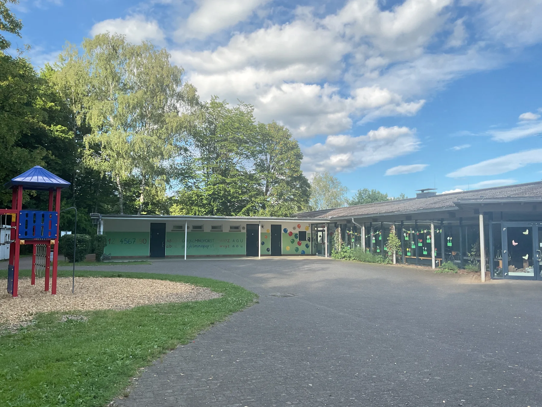 Schulhof der GGS Auf dem Höchsten mit Klettergerüst und Spielgeräten, Schulgebäude und blauem Himmel